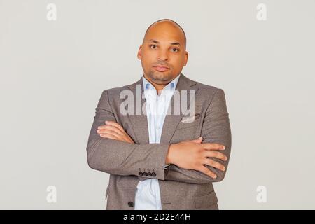 Handsome young male African American businessman in a jacket crossing his arms over his chest, looking at the camera with a flirty facial expression. posing for a photo on a gray background Stock Photo