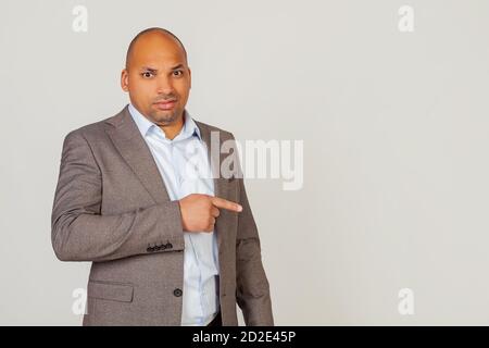 Male African American businessman in a jacket pointing with hand and finger with an expression of disgust. Copy space. on a gray background Stock Photo