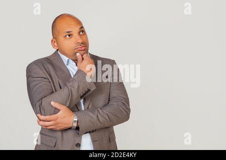Handsome young male African American, businessman in jacket looking to the side and thinking touching chin with hand looking to the side with pensive facial expression. Stock Photo