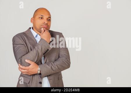 Handsome young male African American, businessman in jacket looking to the side and thinking touching chin with hand looking to the side with pensive facial expression. Stock Photo