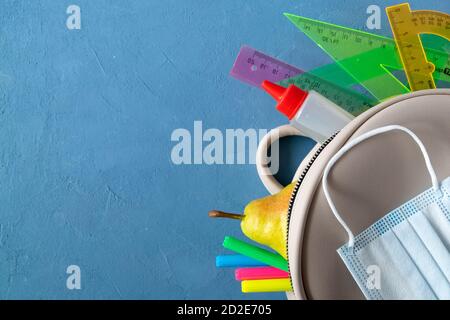 School supplies, school backpack and medical mask on a blue background. Stock Photo