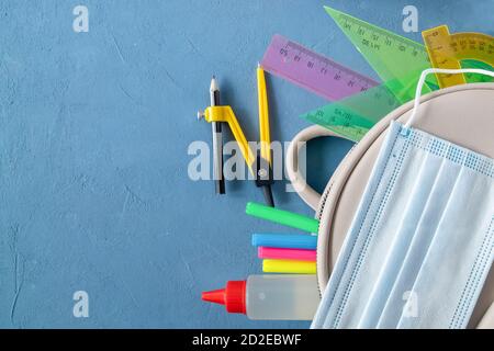 School supplies, school backpack and medical mask on a blue background. Stock Photo