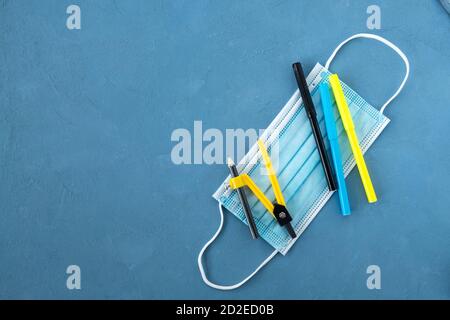 Medical mask, multi-colored markers and compass for drawing on a blue background Stock Photo