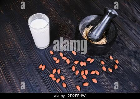 Grinding almonds to make milk. Mortar and pestle with almond flour on black wooden background. Preparation of vegetable milk drink from nuts. Stock Photo