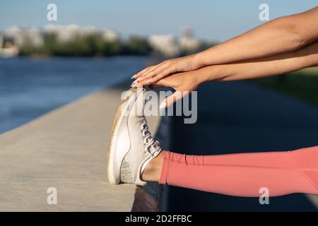 Close up of female stretching muscles making functional training, doing exercises for legs before a work out. Fitness, urban running. Stock Photo