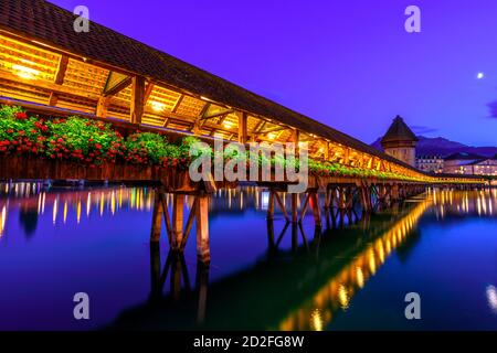 Kapellbrucke historic flowered Chapel Bridge with Water Tower reflects over Reuss river on Lake Lucerne at night. Mount Pilatus mountain overlooking Stock Photo