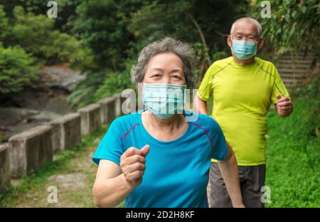 Senior couple wearing face mask and walking trough nature park Stock Photo