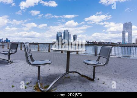 Chairs and table on a promenade along East River in Manhattan with a view of Brooklyn Stock Photo