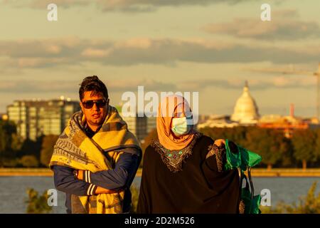 Washington DC, USA, 10/02/2020: A muslim couple is walking on a park at sunset with Capitol Hill Building in background. The man is covering himself w Stock Photo