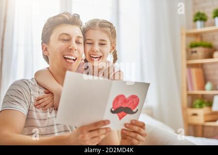 Happy father's day! Child daughter congratulates dad and gives him postcard. Daddy and girl smiling and hugging. Family holiday and togetherness. Stock Photo