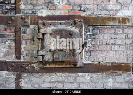 Rusty old metal hatch door of a red brick kiln in an abandoned factory. Rusty metal hatch door with metal frame bolted to old red brick wall. Stock Photo