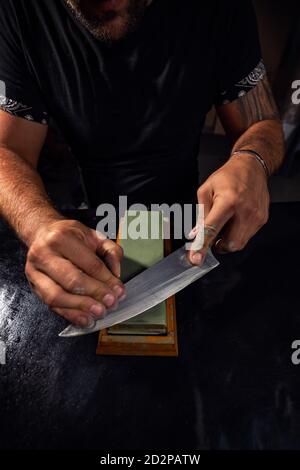 Close up of hands sharpening Japanese chef knife with whetstone Stock Photo