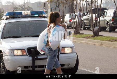 A woman carrying bags of ice walks past a Gulfport police car after receiving items handed out by the National Guard in the parking lot of Crossroads Mall in Gulfport, Mississippi September 1, 2005. Flooding, power outages and storm damage from Hurricane Katrina left the U.S. oil industry in disarray Thursday, as industry and government officials warned it could take months to restore a devastated refining system. REUTERS/Frank Polich  FJP/CCK