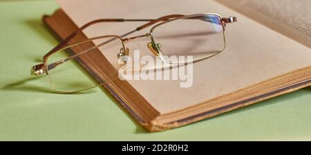 The glasses are lying on an open book on a solid green background Stock Photo