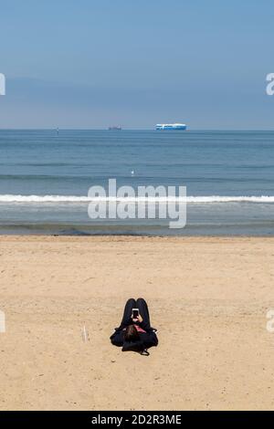 Young woman lies on the beach while using her smart phone. Stock Photo