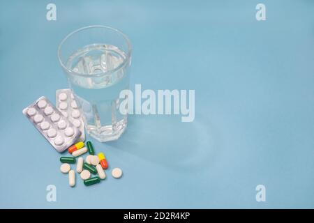 Blister with white pills, transparent glass of water and various pills and capsules are scattered on blue background. Copy space, selective focus. Pha Stock Photo
