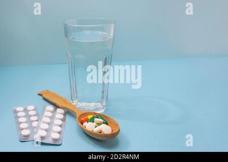 Lot of pills in spoon and glass of water on blue background. Medical concept. Excessive drug use. Copy space, selective focus. Stock Photo