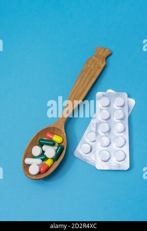 Many different pills and capsules of medicines in wooden spoon on blue background. Copy space, selective focus. The concept of medication Stock Photo