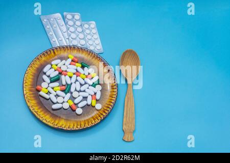 Many different pills and capsules of medicines on dark plate. Wooden spoon on light blue background. The concept of overuse medicines, antibiotics Stock Photo