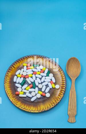 Many pills and capsules of medicines on dark plate and spoon. Blue background, copy space. Medicine, pharmacy, treatment concept. Stock Photo