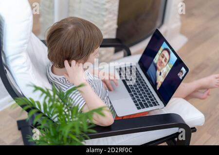 Happy kid boy sit on chair with computer using laptop having a video call with father. Child talking to his dad and dog on video chat Stock Photo