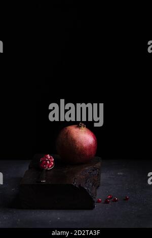 Fresh whole pomegranate and seeds in spoon arranged on wooden board in dark studio on black background Stock Photo