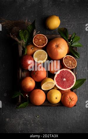Top view of various ripe citrus fruits and green leaves on wooden tray placed on table Stock Photo