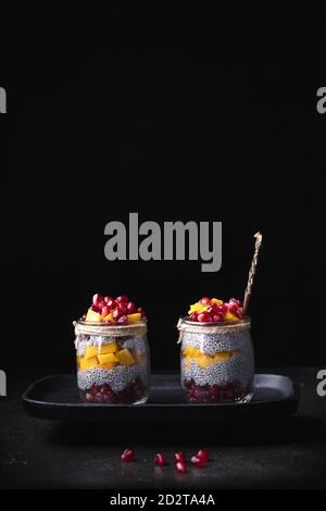 Glass jars with various tropical fruits placed on tray on table on black background in studio Stock Photo