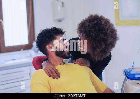 Young African American female smiling and looking at bearded Hispanic man while visiting dentist together Stock Photo