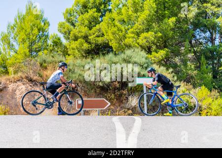 Low angle side view of male and female bikers in sportswear standing face to face with bicycles on asphalt road near forest while choosing direction f Stock Photo