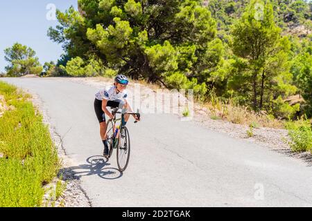 Full length of strong female bicyclist riding bike on curvy paved road going up among mountains Stock Photo