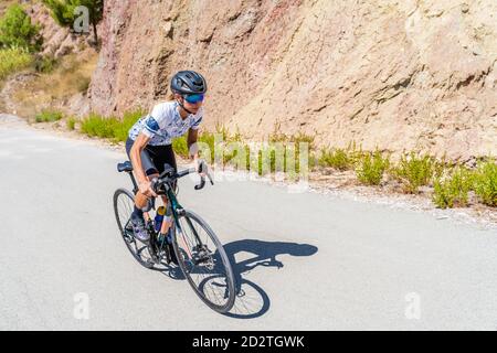 Full length of strong female bicyclist riding bike on curvy paved road going up among mountains Stock Photo