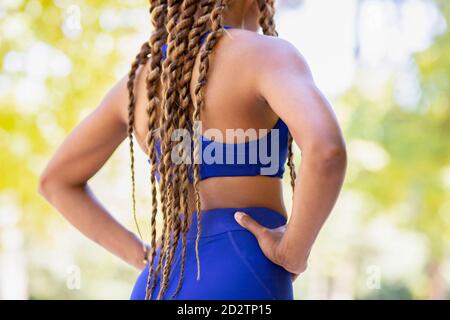 Low angle back view of crop unrecognizable ethnic female athlete standing with hands on waist in park in summer during workout Stock Photo