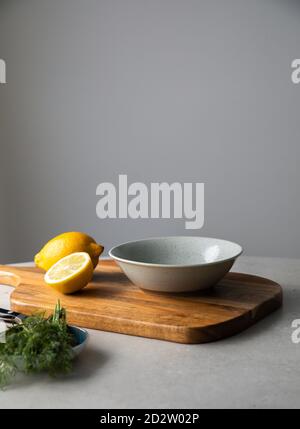 Fresh cut lemon and bunch of green dill placed with bowl and wooden cutting board on kitchen table during cooking Stock Photo