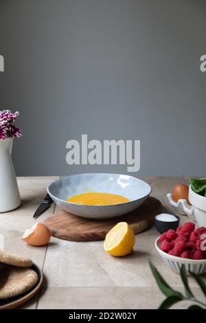 Bowl with mixed eggs placed near fresh berries and lemon on kitchen table with ingredients for recipe Stock Photo