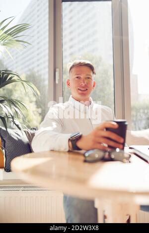 Content businessman sitting at table in modern workplace looking at camera while waiting for meeting Stock Photo