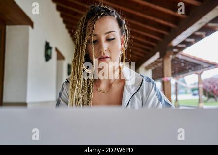 Concentrated female entrepreneur with stylish braids sitting at table with laptop and working remotely in cafe Stock Photo