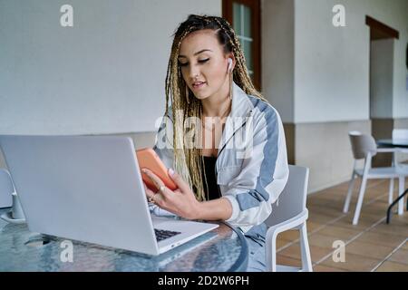 Content female freelancer sitting at table with laptop in cafe and using smartphone while working on business project Stock Photo