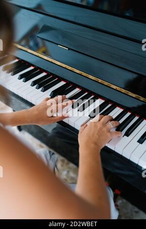 Back view of talented ethnic female musician playing piano while sitting in modern apartment and rehearsing Stock Photo