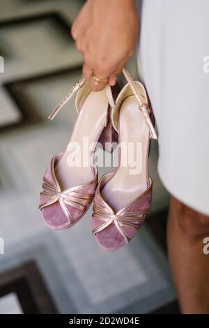 High angle of crop anonymous female standing with pair of elegant high heeled shoes on blurred background of floor in shop