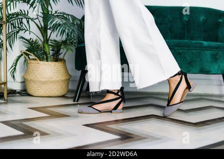 Side view of anonymous crop female wearing wedge sandals and trendy jeans standing in modern flat Stock Photo
