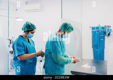 Side view of vet doctors putting on protective uniform and gloves while standing in bright operating theater of veterinarian hospital and preparing for surgery Stock Photo