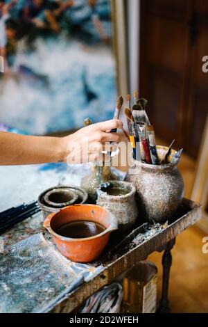 anonymous female artist taking paintbrush from pot with various brushes in art workshop Stock Photo