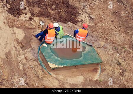 Workers in orange overalls and helmets on a smoke break, top view. Stock Photo