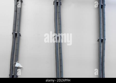 Wires on the wall in a protective round metal casing. Corrugated grey pipes for wire laying Stock Photo