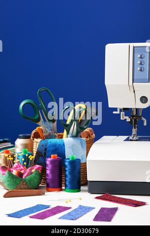 Sewing accessories in a basket and spools of threads next to a sewing machine Stock Photo