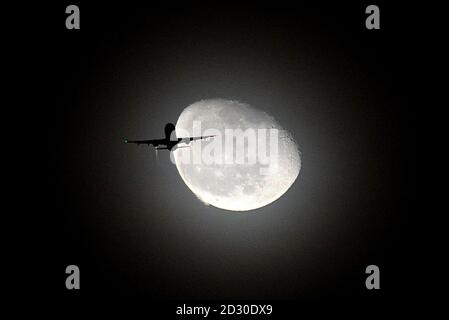 An airliner is seen passing in front of the moon above Craven Cottage during the match Stock Photo