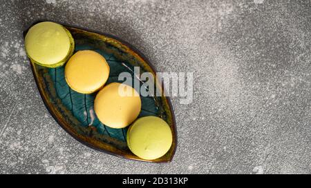 Top view of tasty piled yellow and green macaroons on beautiful green leaf plate. Pistachio and passion fruit cakes. High quality photo Stock Photo