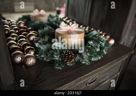 Round craft gift box with pink ribbon, bow, stands on a wooden table in a coniferous garland lights, slice of Christmas tree golden balls. copy space Stock Photo