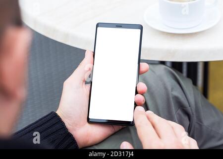 Close up of man's hands holding mobile smart phone with blank copy space screen. Image of man sitting at a table with a coffee in cafe and using mobil Stock Photo